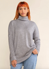 This is a nearly full length picture of a model. She is wearing a light long sleeve turtle neck sweater in a heather grey.