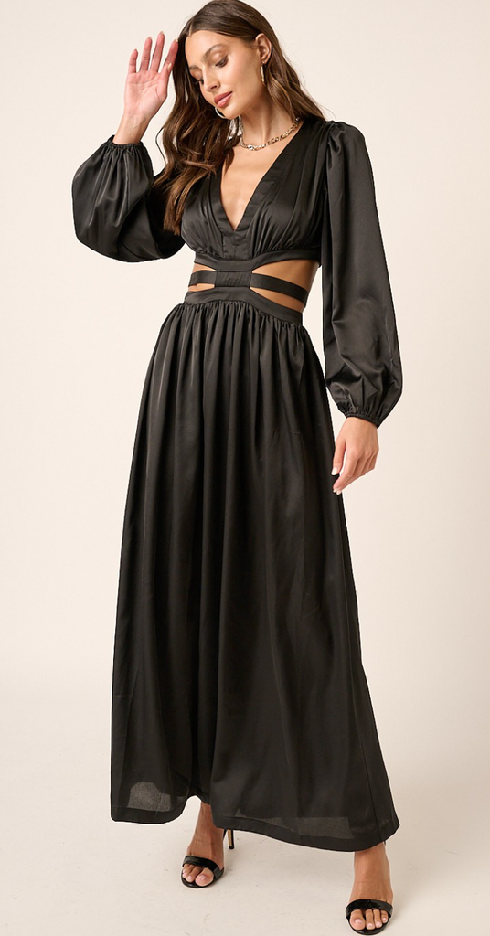 A brunette woman wears a black satin maxi dress. The dress has cut outs at the waistline.