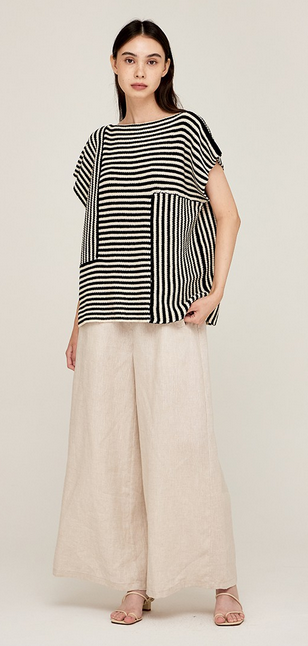 This is a full length picture of a model. She is wearing an oversized boxy short sleeve top in cream and black. The top has stripes going in different directions on different sections of it.