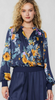 This is a picture of a model from the waist up. She's wearing a satin long sleeve blouse in navy blue. It has a v shaped neckline. The shirt is printed in a floral pattern in gold, light purple, and shades of light blue.
