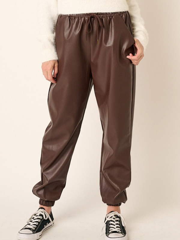 A woman wears faux leather joggers in a chocolate brown.