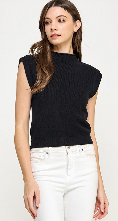 This is a nearly full length picture of a model. She's wearing a short sleeve mock neck sweater in black. She has it paired with white denim pants.