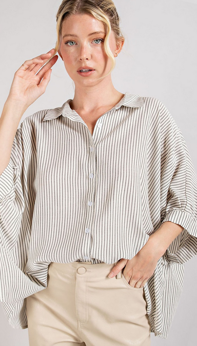 This is a picture of a model from the waist up. She's wearing a short sleeve white button up shirt that has thin vertical black stripes. The shirt has an oversized fit.