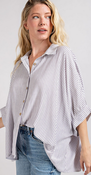 This is a picture of a model from the waist up. She's wearing a short sleeve white button up shirt that has thin vertical navy stripes. The shirt has an oversized fit.