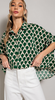 A blonde caucasion woman wears a kelly green top with a ivory scalloped pattern printed on it. The shirt is a button up in an oversized fit.