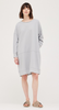 This is a full length picture of a model. She is wearing a long sleeve dress that stops above her knee. The dress has a raw edge neckline. The fabric is a soft sweatshirt like cotton and is a soft grey color.