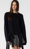 This is a nearly full length picture of a model. She's wearing a long sleeve navy sweater, The sweater has two ribbon like bows on the front bottom hem and on the back bottom hem.