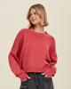A woman wears a slightly cropped long sleeve sweater in a berry color.