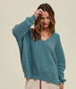 This is a picture of a model from the waist up. She is wearing a very soft oversized long sleeve sweater in a dusty blue. The sweater has a v neckline.