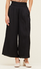 A picture of a model from the waist down. She's wearing black wide leg pants with a smocked waist. The pants are a satin fabric.