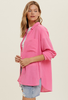 This model is wearing a bright pink button down shirt as a layering piece. The fabric is slightly textured. She has the long sleeves pulled up a bit.