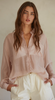 A model is wearing a sheer light pink button down shirt. She has it paired with white pants with a front pleated detail.